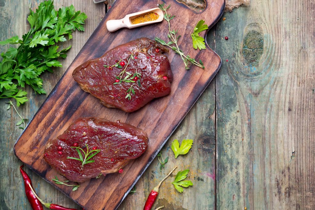 Marinating meat with spices and greenary on wooden table, copy space flat lay